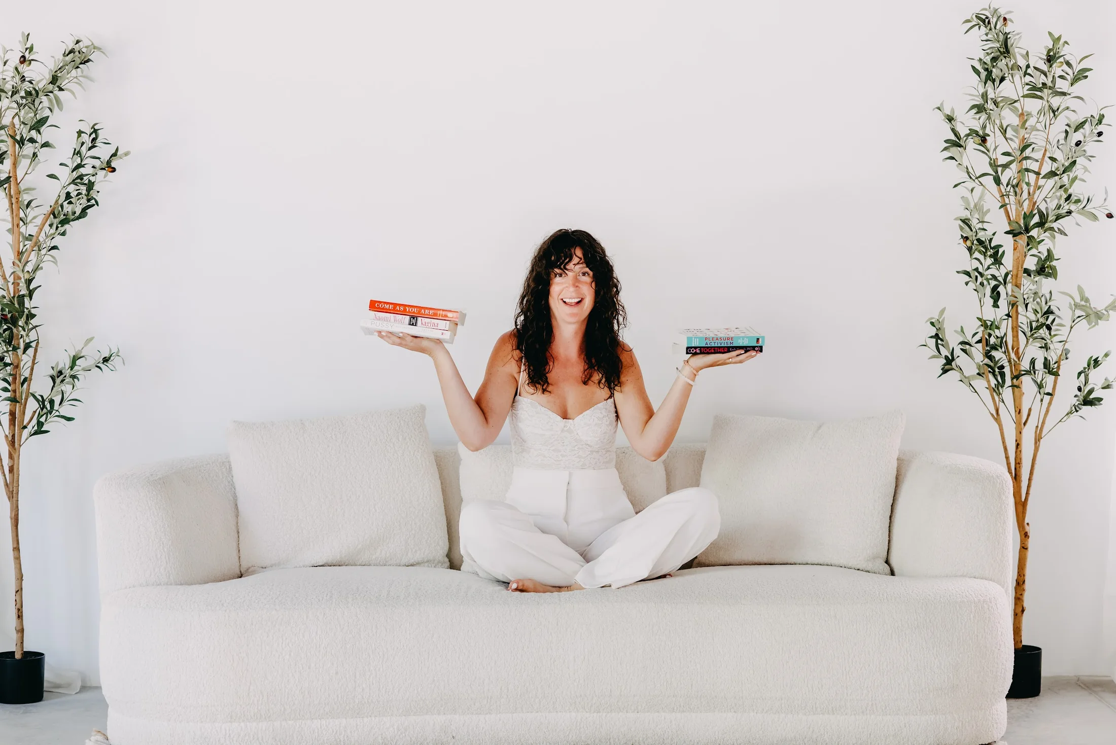 Shelby Foster smiling on a cream sofa with books in both hands